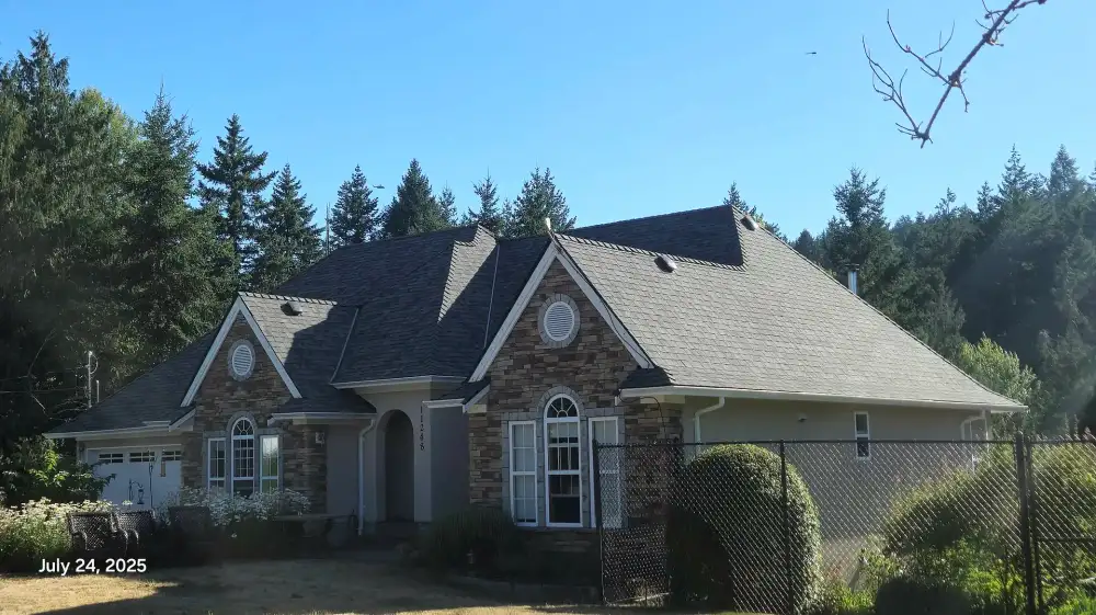 House with a stone facade and a steep roof, surrounded by trees under a clear sky. July 24, 2025.
